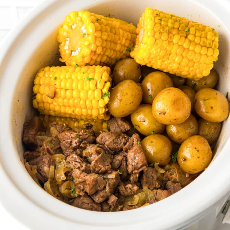 Wide view of a square view of steak pieces, potatoes and corn in a slow cooker cooked.