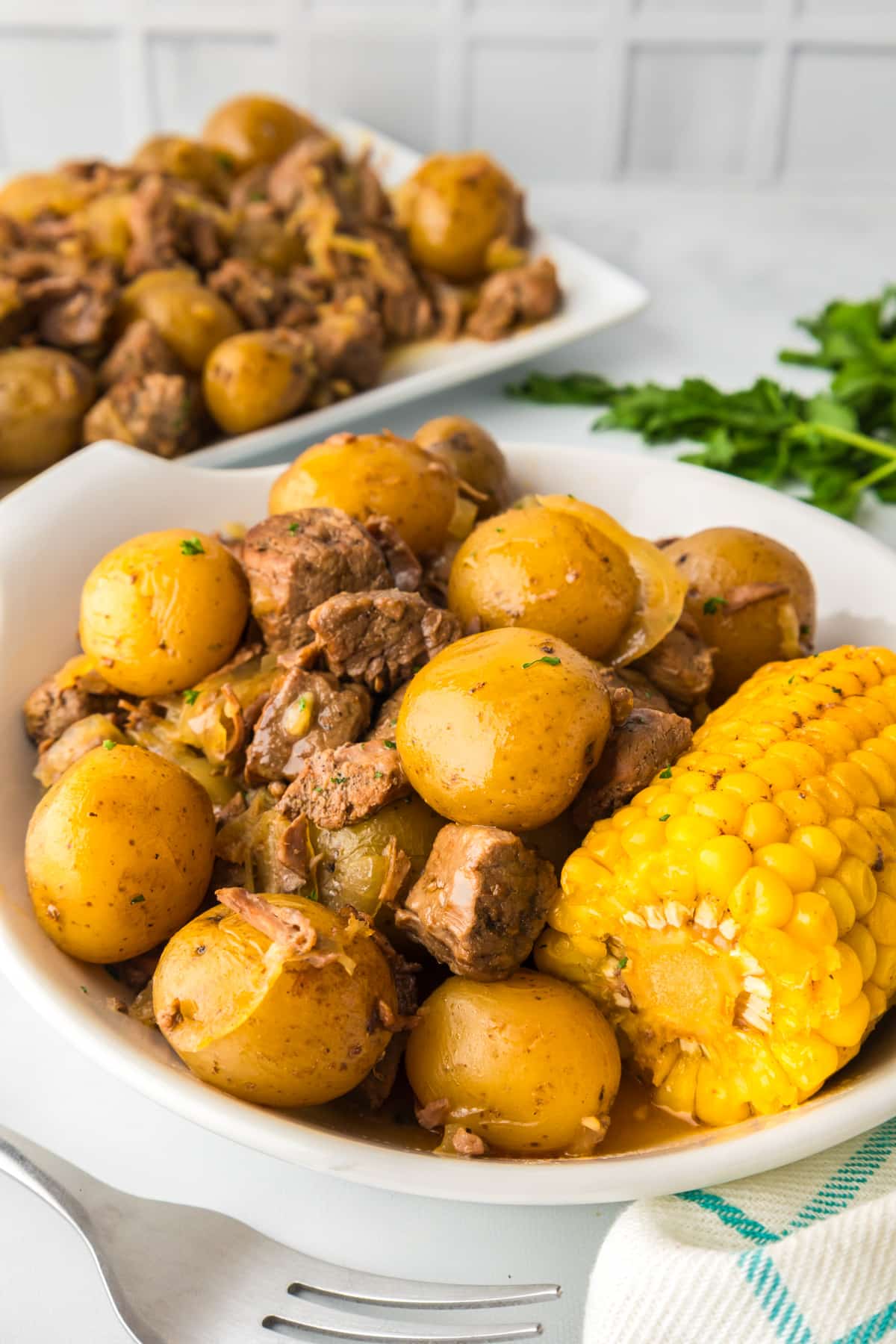 A plate filled with steak, potatoes and a piece of corn with more on a platter behind.