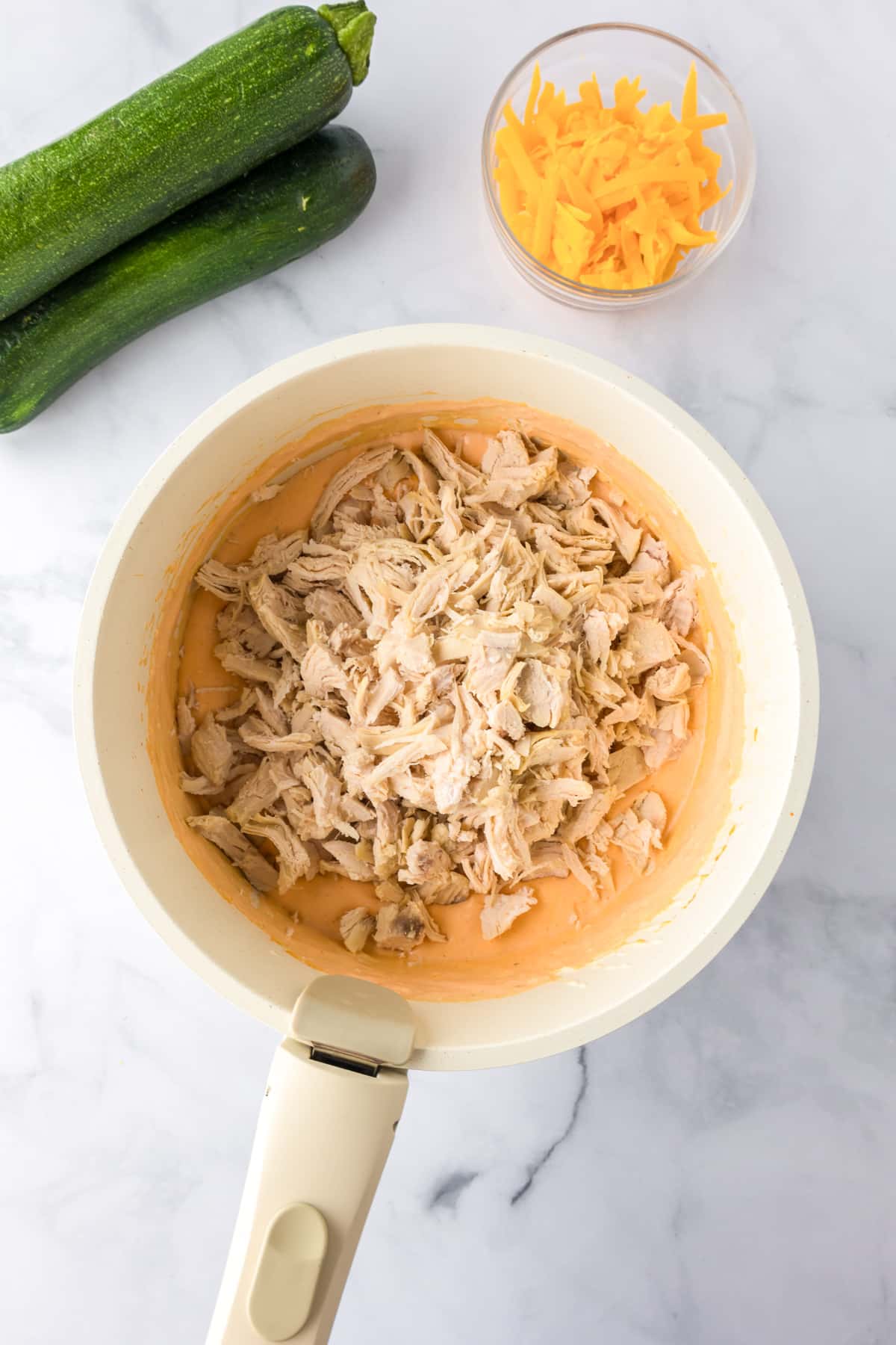 A white pan with shredded chicken being mixed into a creamy buffalo cause for buffalo chicken zucchini boats.