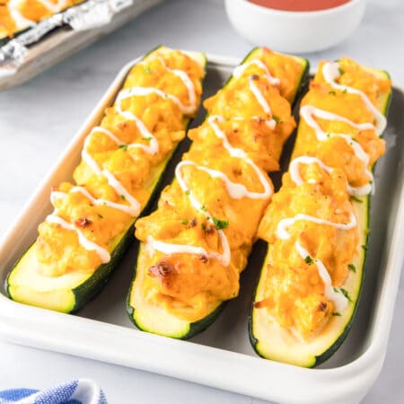There buffalo chicken zucchini boats on a platter drizzled with ranch dressing.