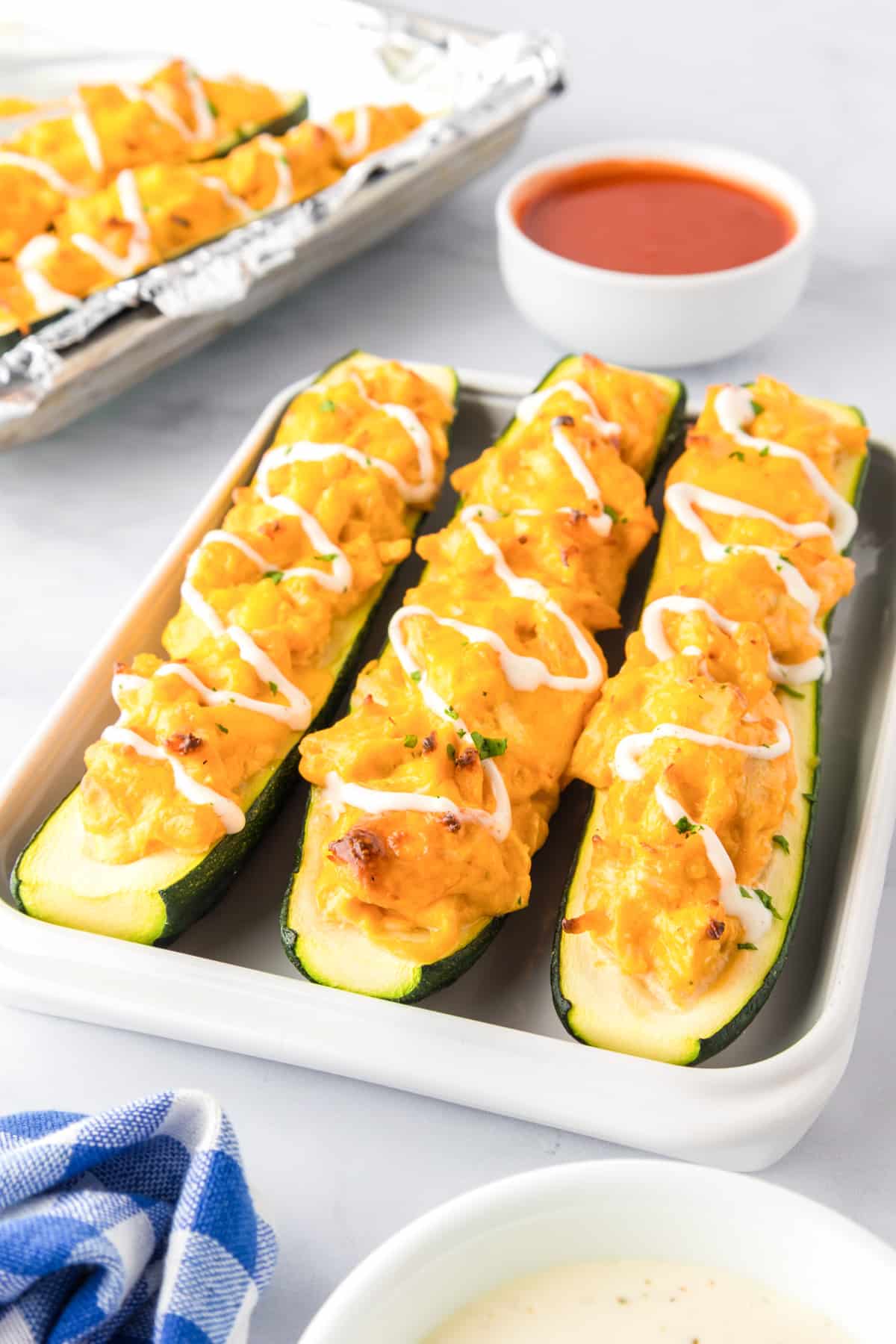 Zucchini halves stuffed with a buffalo chicken cheesy mixture for buffalo chicken zucchini boats with more on a pan in the background.