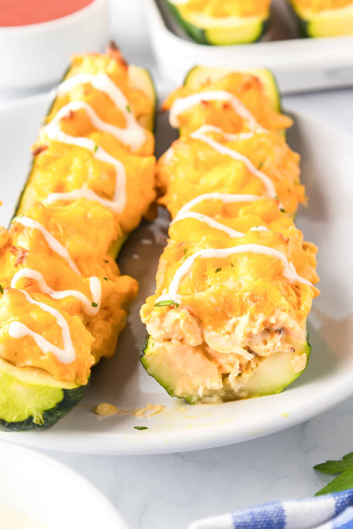 Two zucchini boats filled with a buffalo chicken mixture from the edge where you can see the layers on a plate.