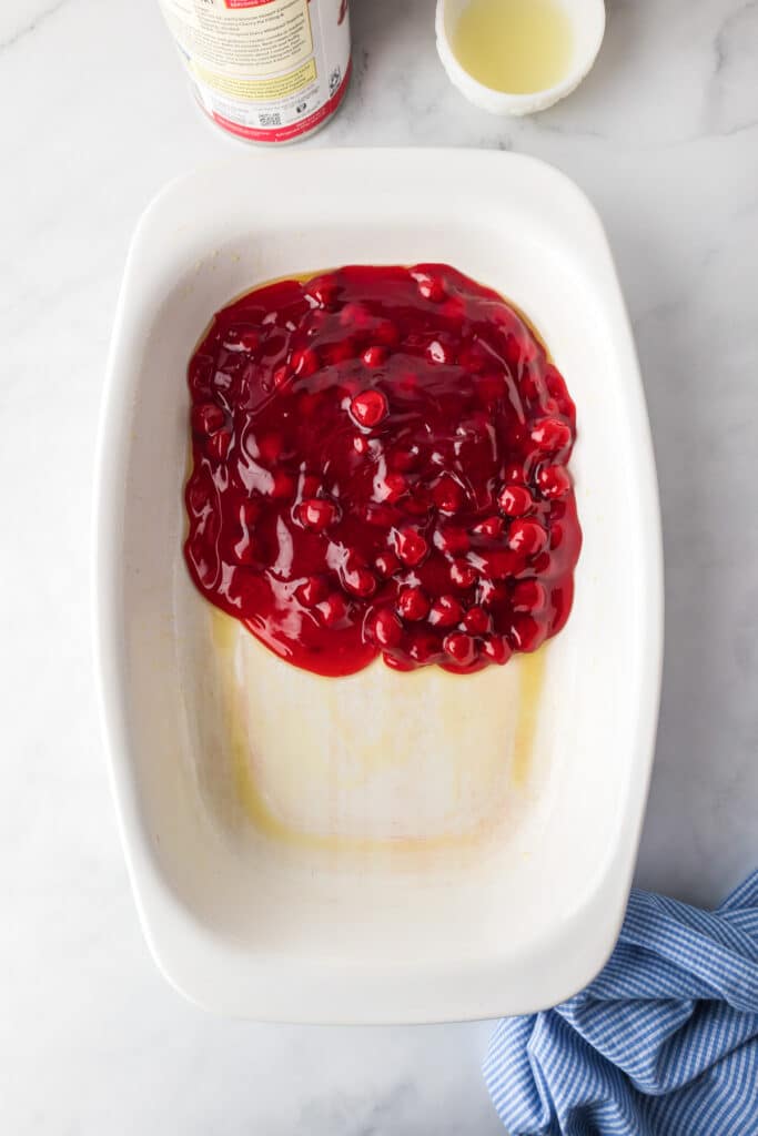 Cherry pie filling being added to an oiled pan on a counter.