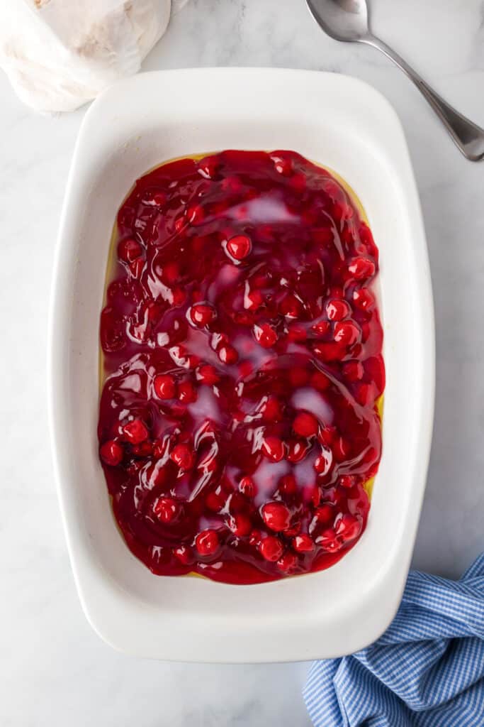 A white baking dish filled with cherry pie filling on a counter.