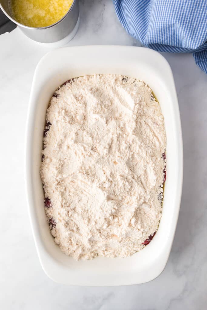A white casserole dish full of dry white cake mix over cherry pie filling.