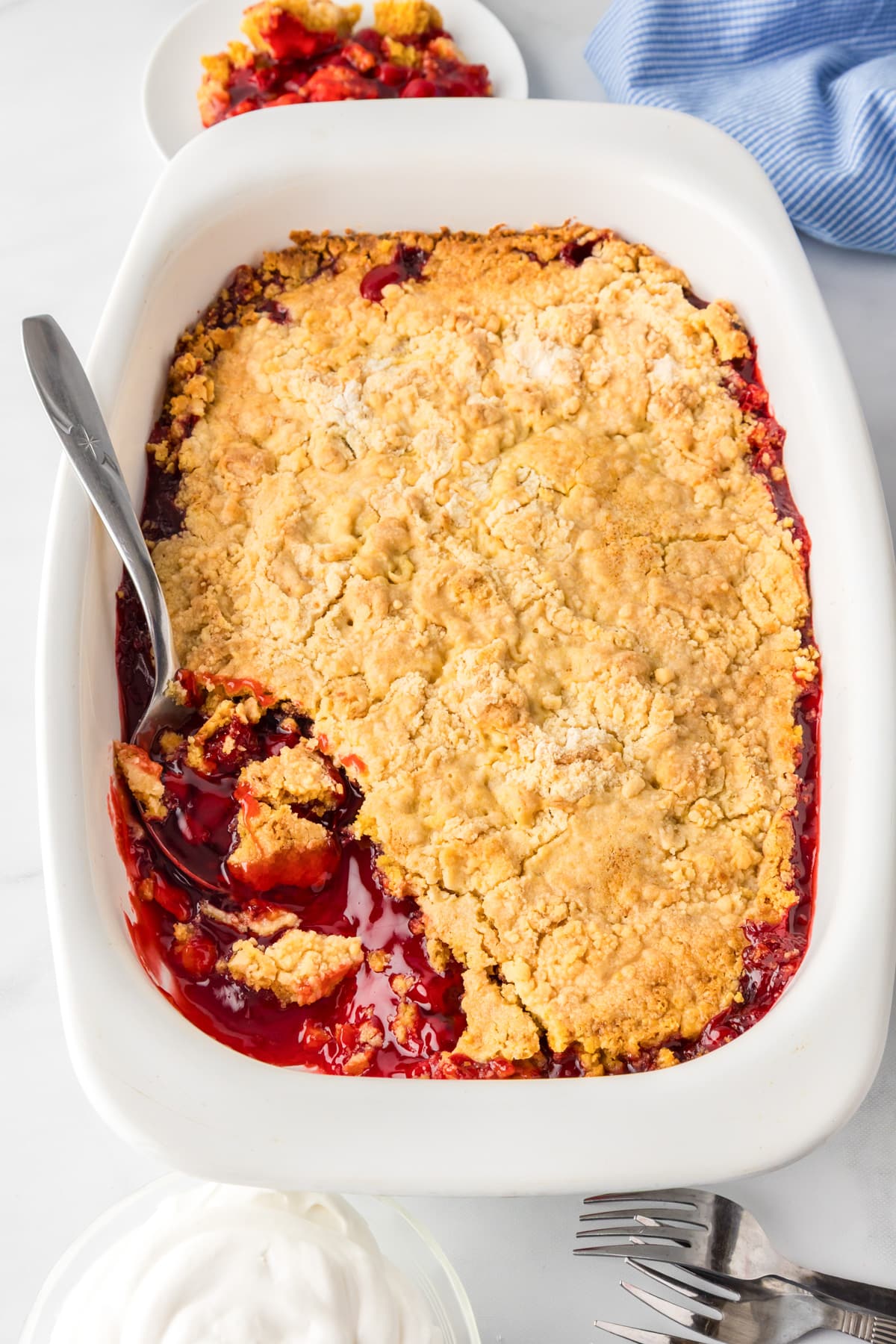 A baked cherry dump cake in a casserole dish with a spoon scooping a gooey scoopful.