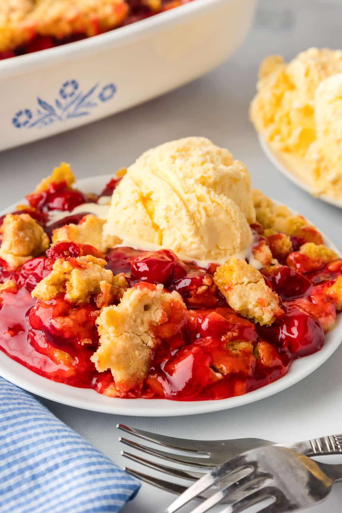 A plate of cherry dump cake topped with cold ice cream melting into the warm dessert.