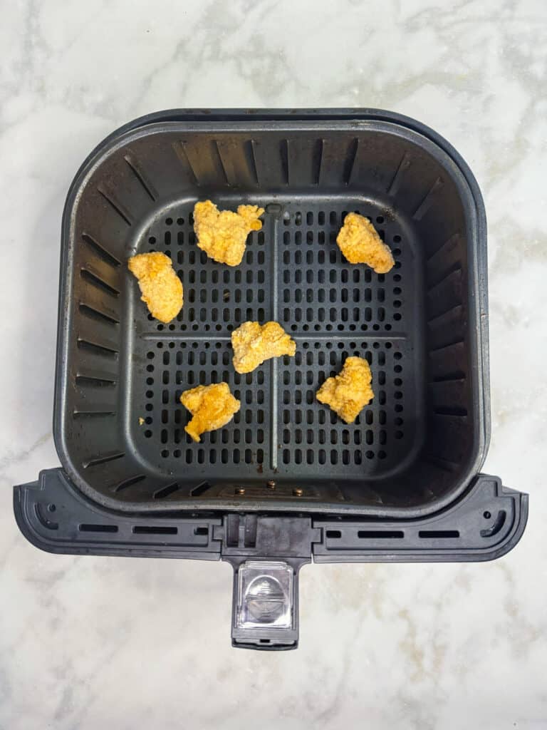 Frozen chicken nuggets in an air fryer base for a chicken nugget wrap.