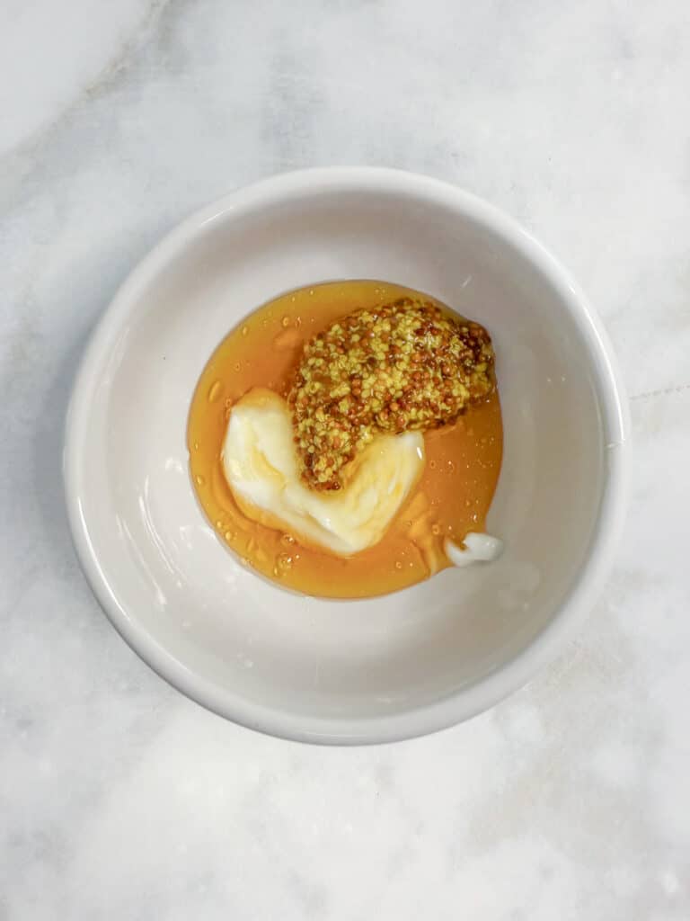 A white bowl containing honey, whole grain mustard, and mayonnaise to make a honey dijon sauce for chicken nugget wraps.