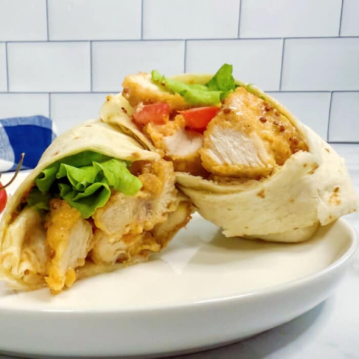 A chicken nugget wrap cut in half, filled with breaded chicken, lettuce, tomato, and a honey mustard sauce.