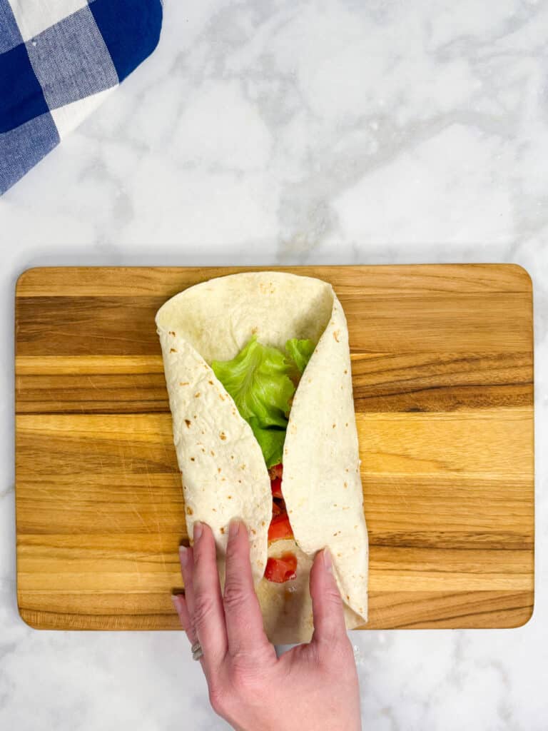 A hand is folding the side of a tortilla in to roll up a chicken nugget wrap/
