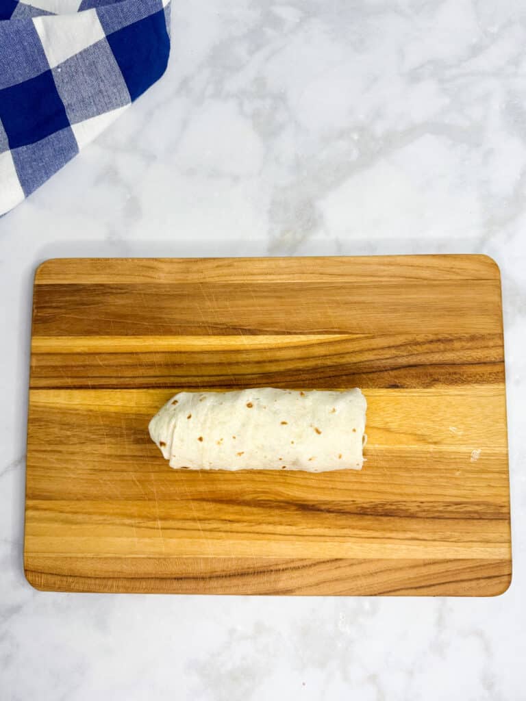 A single rolled chicken nugget wrap on a cutting board.