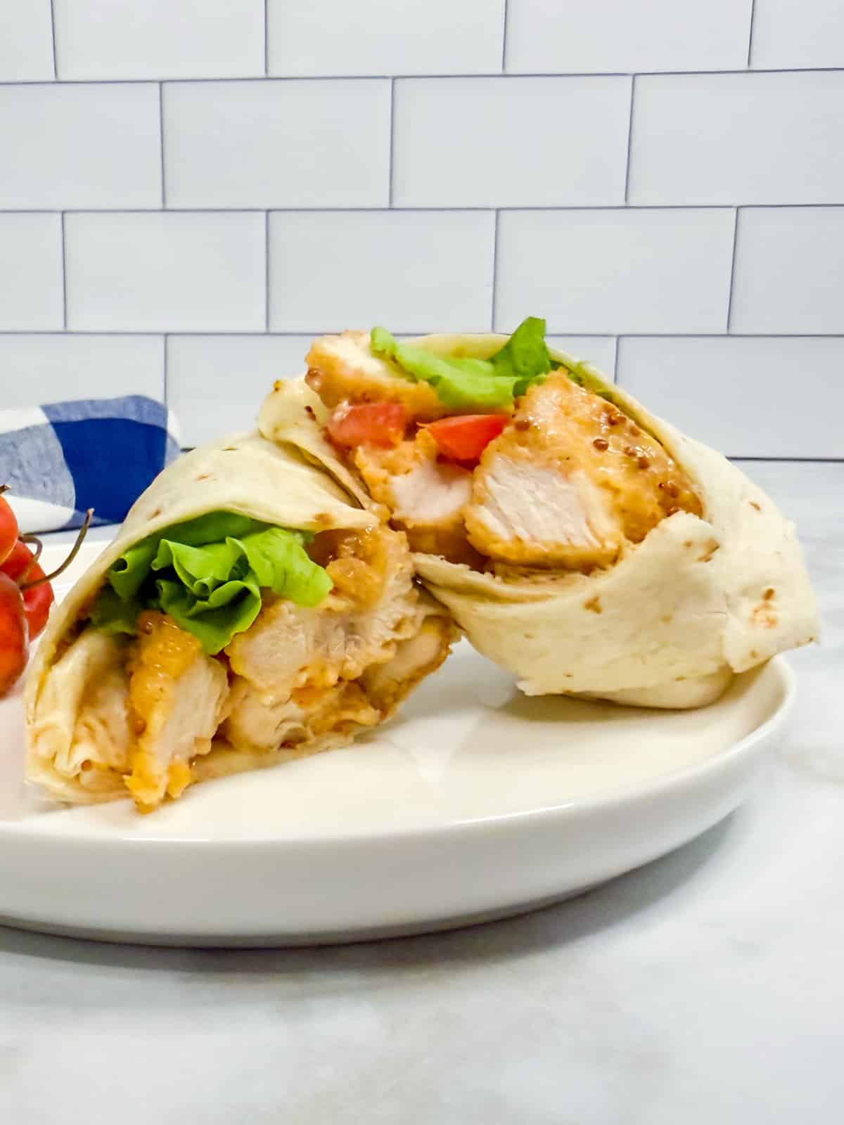 A sliced chicken nugget wrap with lettuce and tomato is displayed on a plate.