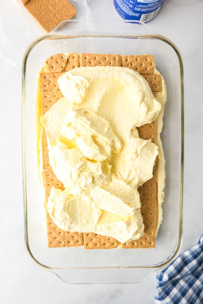 A glass baking dish full of two layers of graham crackers and cream layers for no bake chocolate eclair cake.