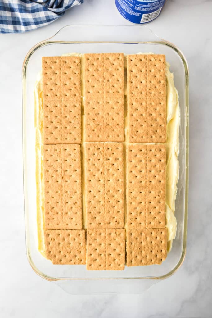A glass baking dish full of three layers of graham crackers and two cream layers with graham crackers on tops for no bake chocolate eclair cake.
