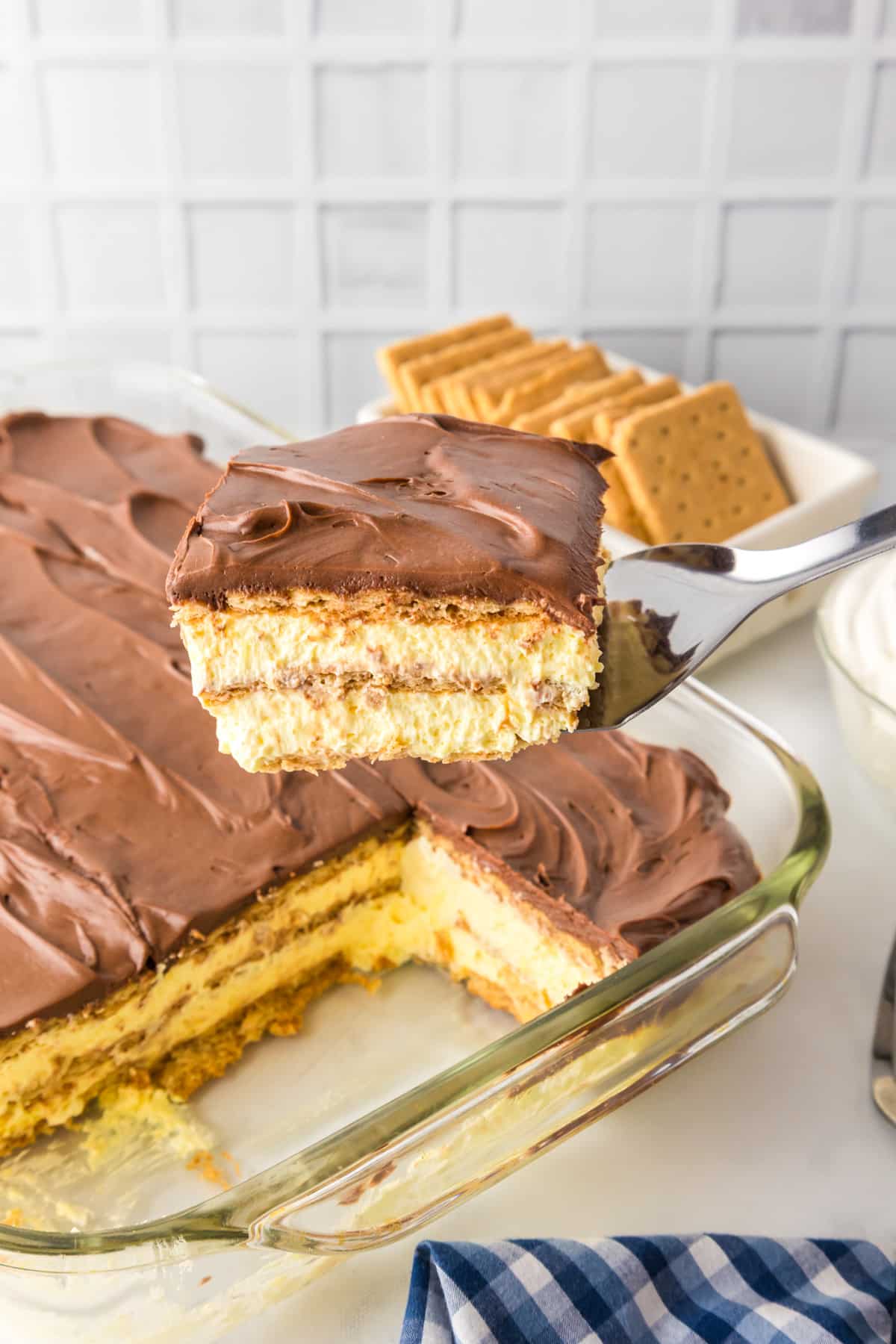 A close-up of a a slice of chocolate eclair cake being lifted by a spatula from a baking pan.