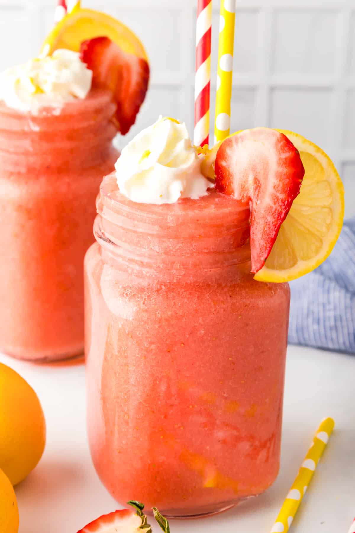 Two mason jars filled with pink frozen strawberry lemonade topped with dollops of whipped cream and fresh berries.