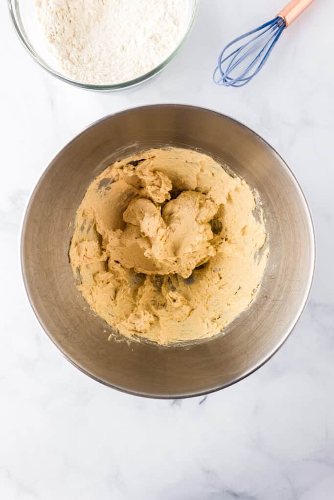 A metal mixing bowl with wet ingredients mixed together for red white and blue M&M cookie dough with the dry flour ingredients in a bowl nearby.