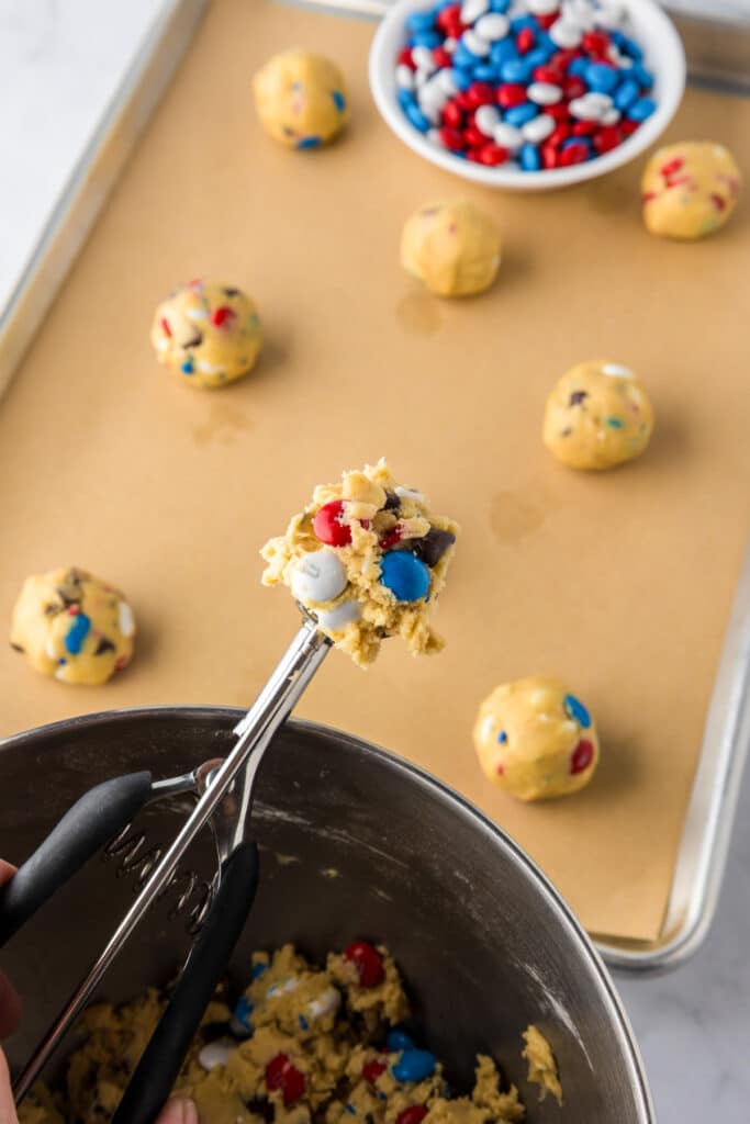 A cookie scoop holds raw cookie dough with red, white, and blue candies being portioned for Red White And Blue M&M cookies.