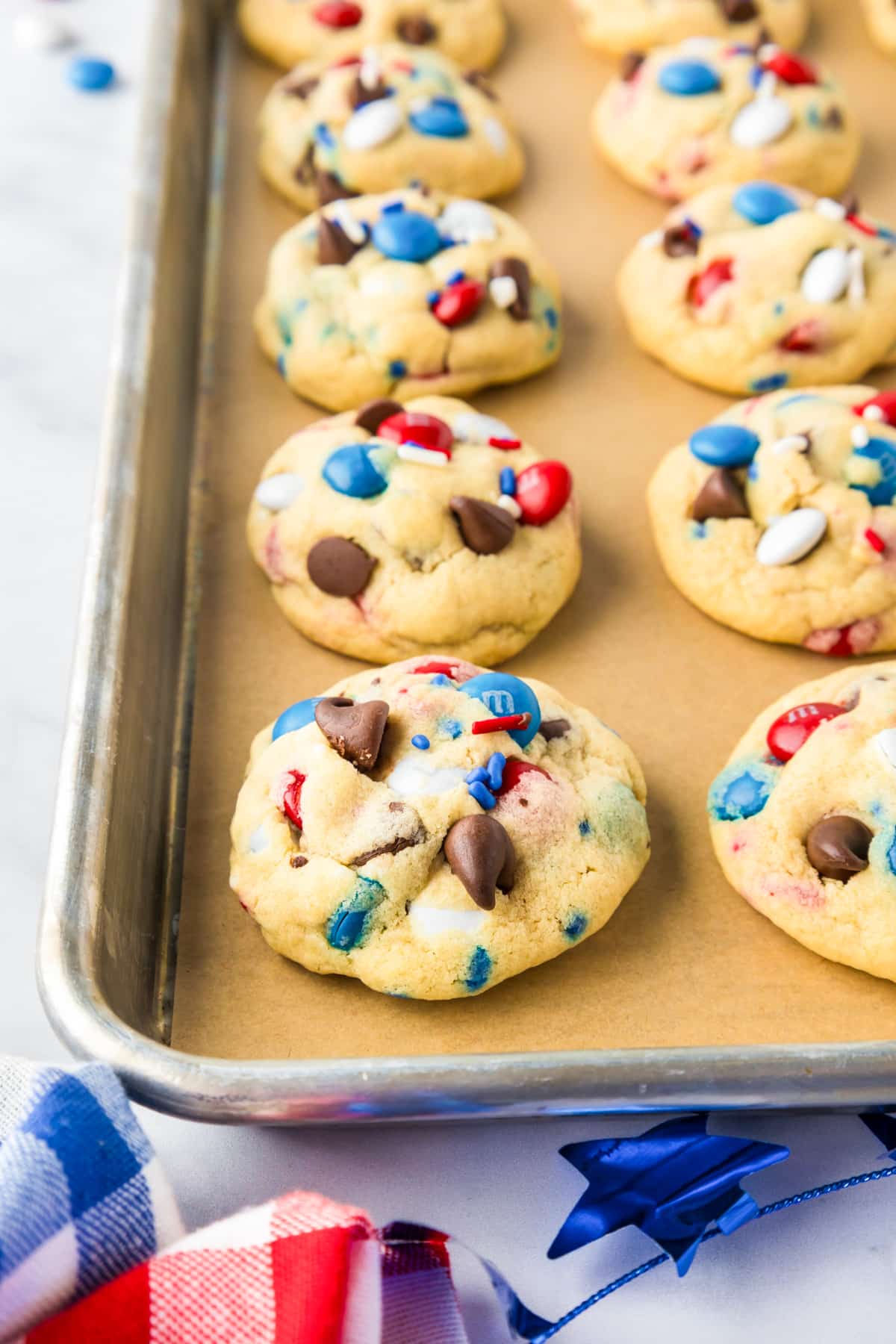 A baking sheet with red white and blue M&M cookies after baking in rows close up from the edge of the pan.