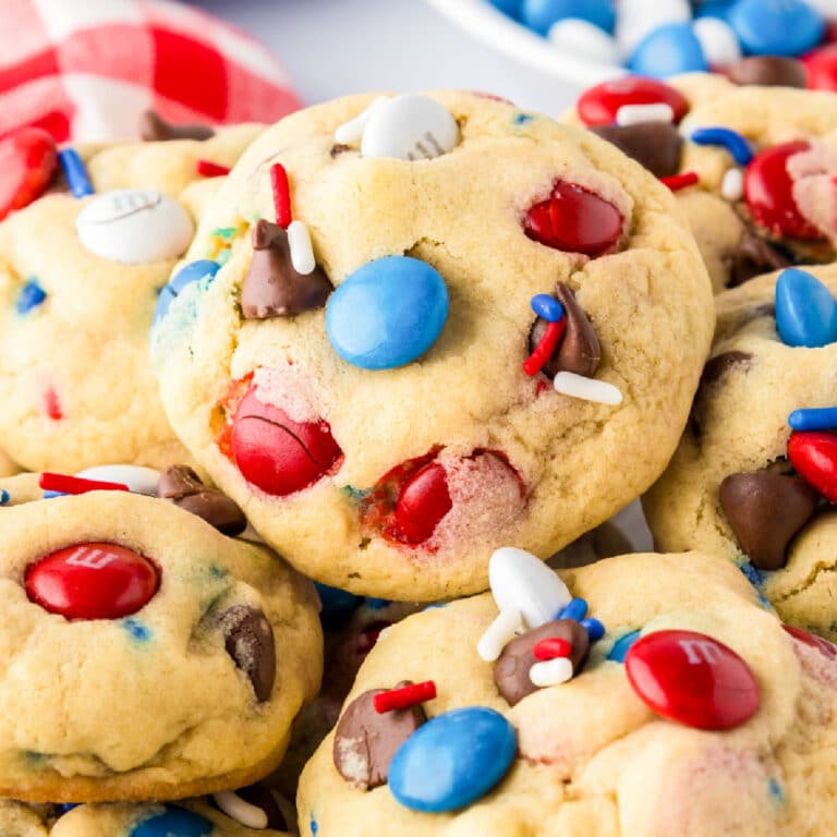 A close-up of cookies with red, white, and blue M&M cookies piled high on a plate.