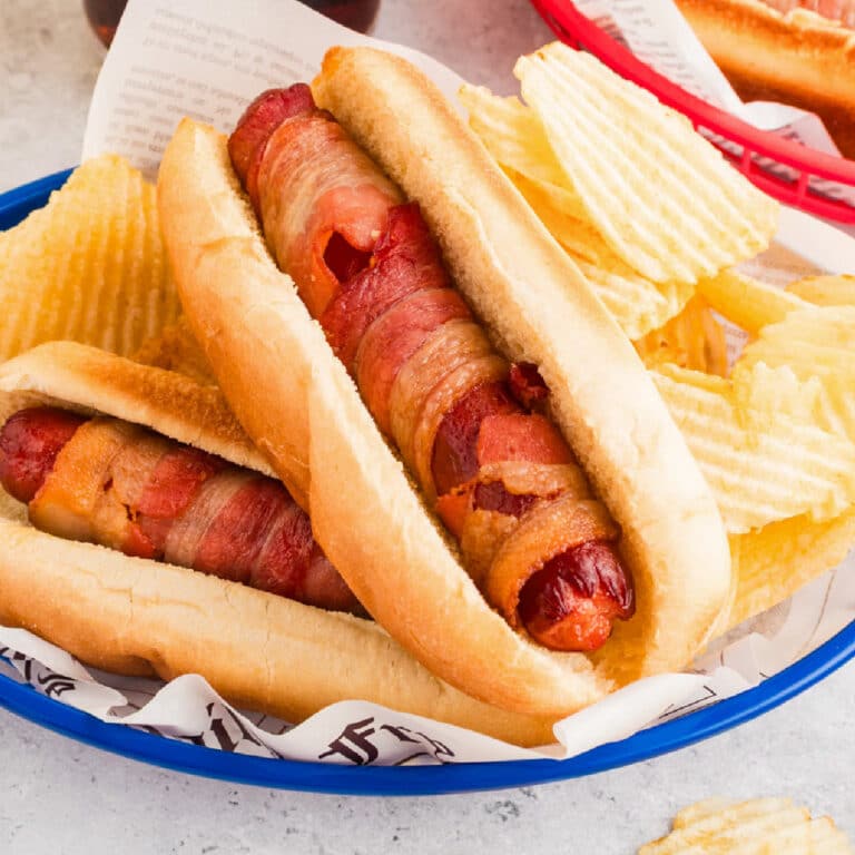 Two bacon-wrapped air fryer hot dogs in buns served in a blue basket with wavy potato chips on the side.