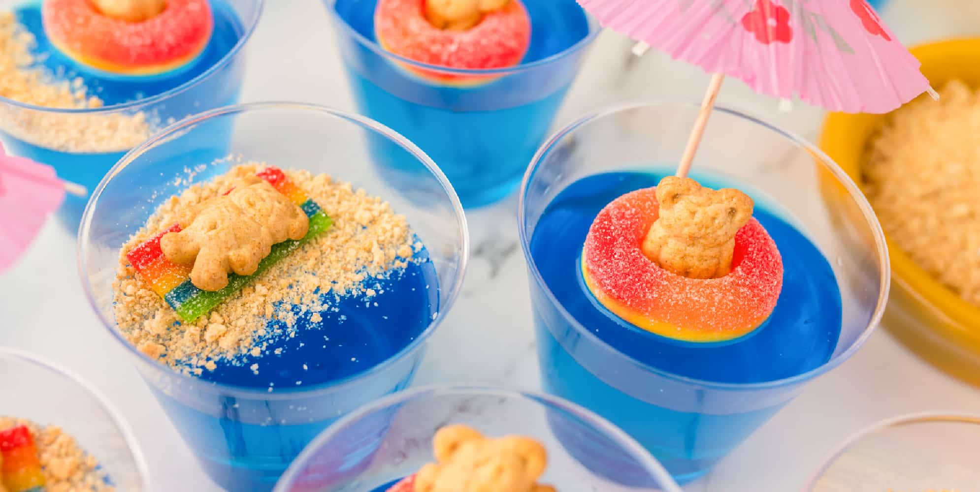 blue jello in a cup with a candy ring and teddy graham