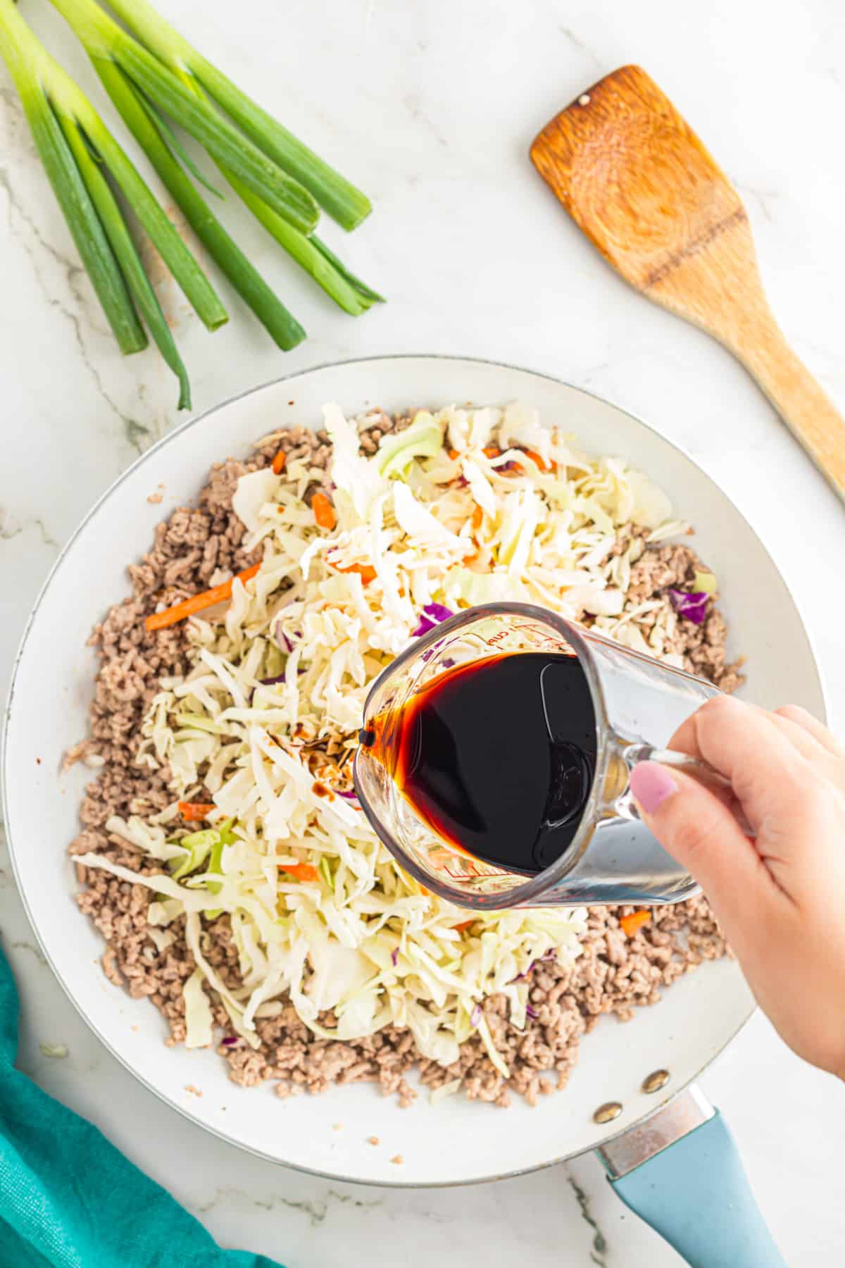 Soy sauce being poured over cabbage and ground pork for egg roll in a bowl.