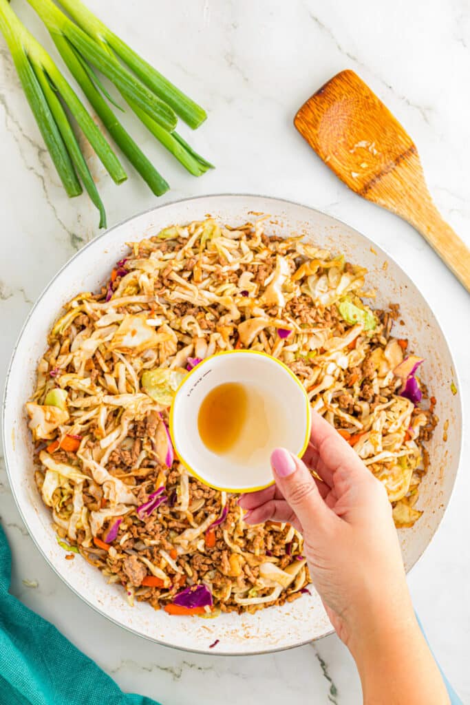 Sesame oil being added to a pan of egg roll in a bowl.