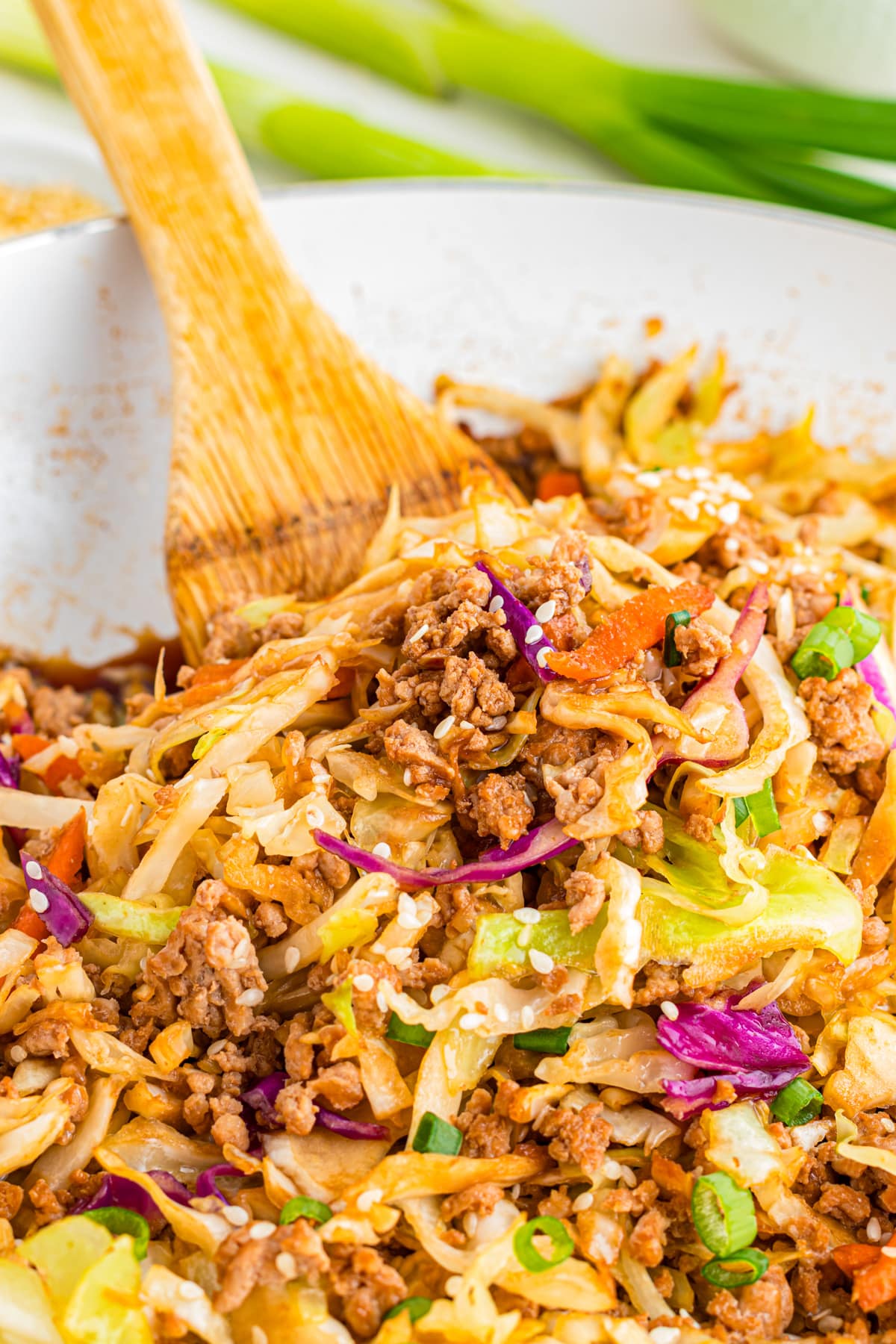 A wooden spoon stirs ground pork and cabbage mixture after making egg roll in a bowl in a pan.