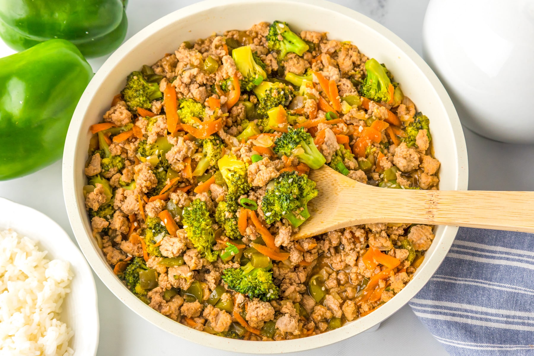A skillet filled with ground turkey teriyaki being scooped with a wooden spoon.