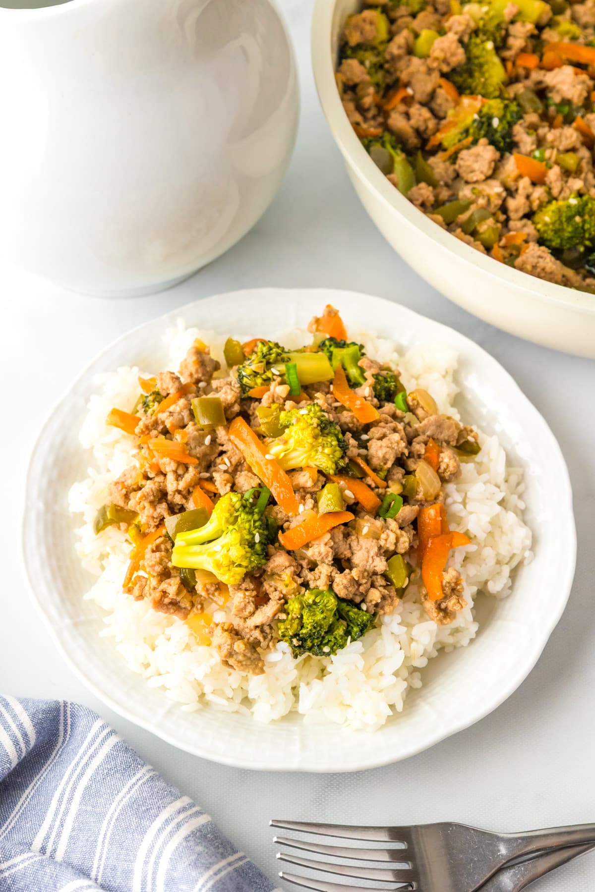 A plate of white rice topped with ground turkey teriyaki with more in a pan nearby.