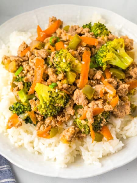A square view of a plate of white rice topped with ground turkey teriyaki and vegetables.