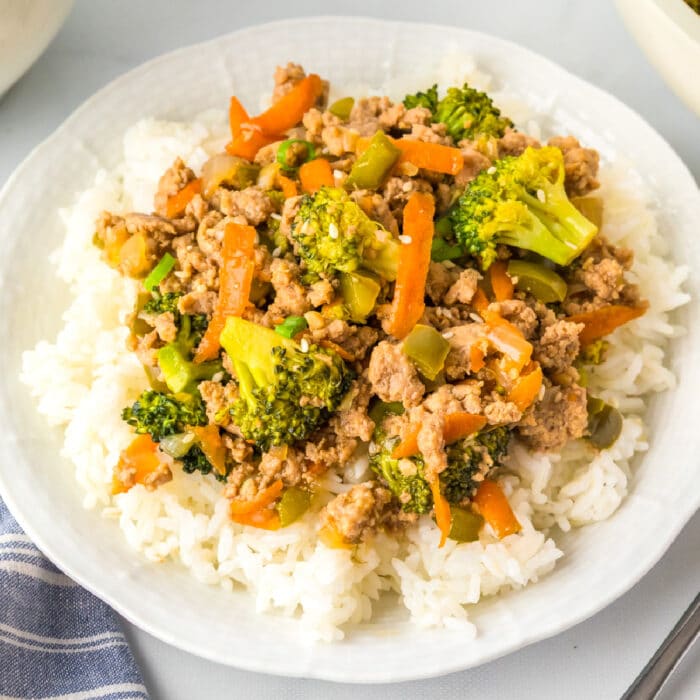 A square view of a plate of white rice topped with ground turkey teriyaki and vegetables.