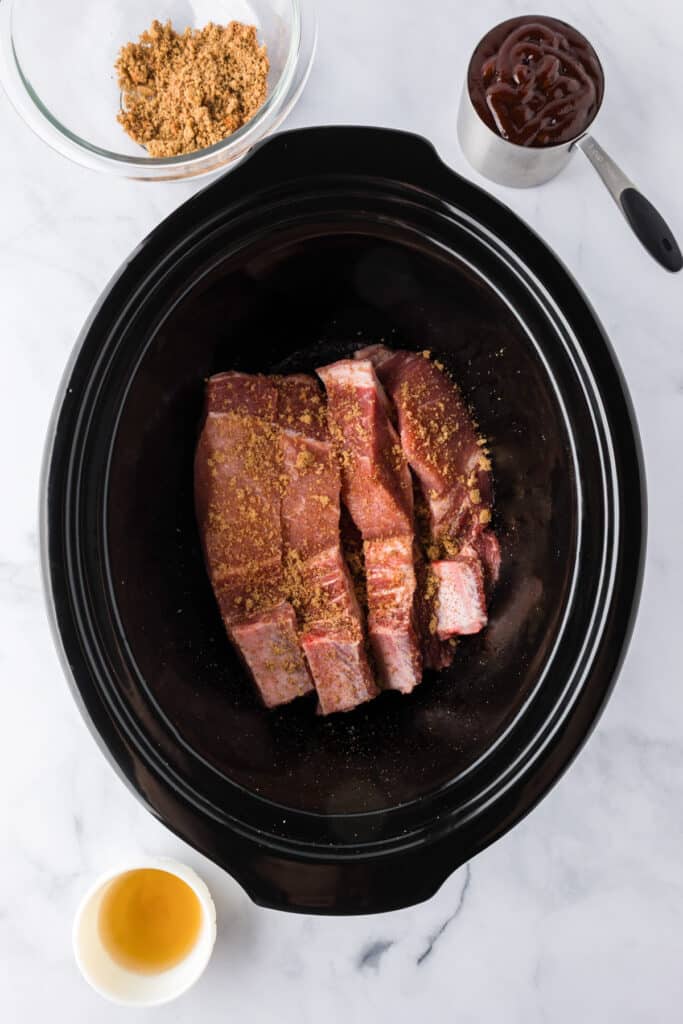 Raw pork loin country style ribs coated with dry rub seasoning in a slow cooker.