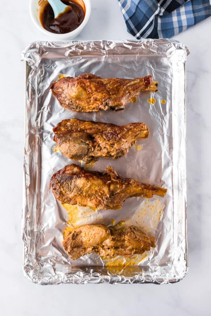 Four cooked loin country style ribs on a foil lined pan being coated with additional bbq sauce.