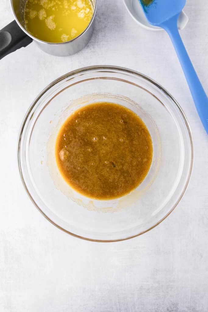 A glass bowl with all wet ingredients mixed except melted butter which is in a small bowl nearby for zucchini brownies.