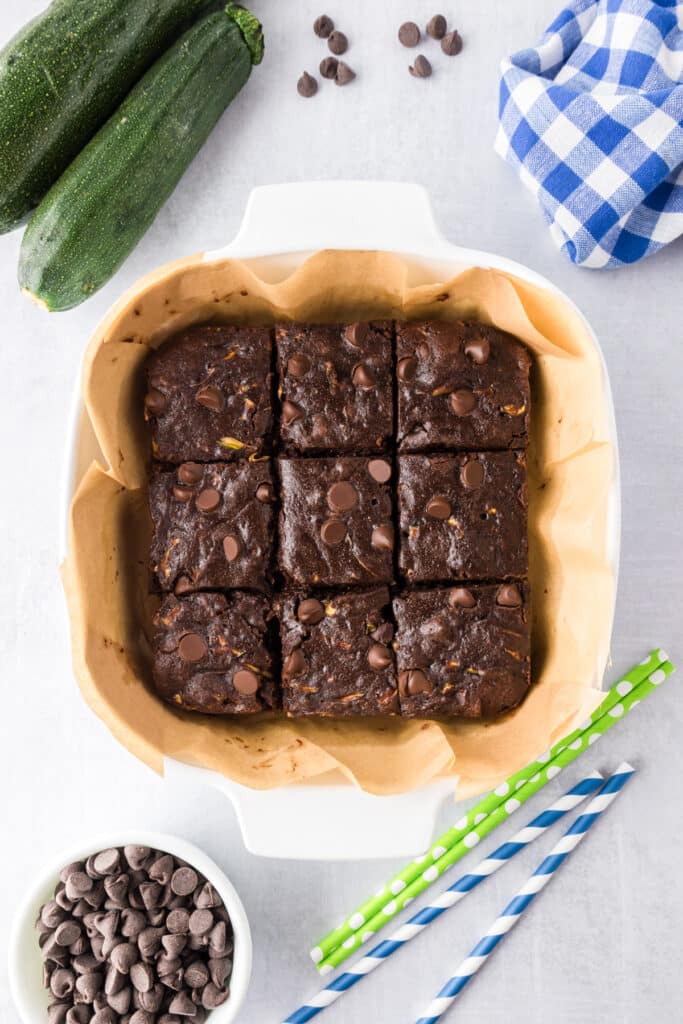 A baking dish with nine chocolate chip brownies on parchment paper sliced in the pan.