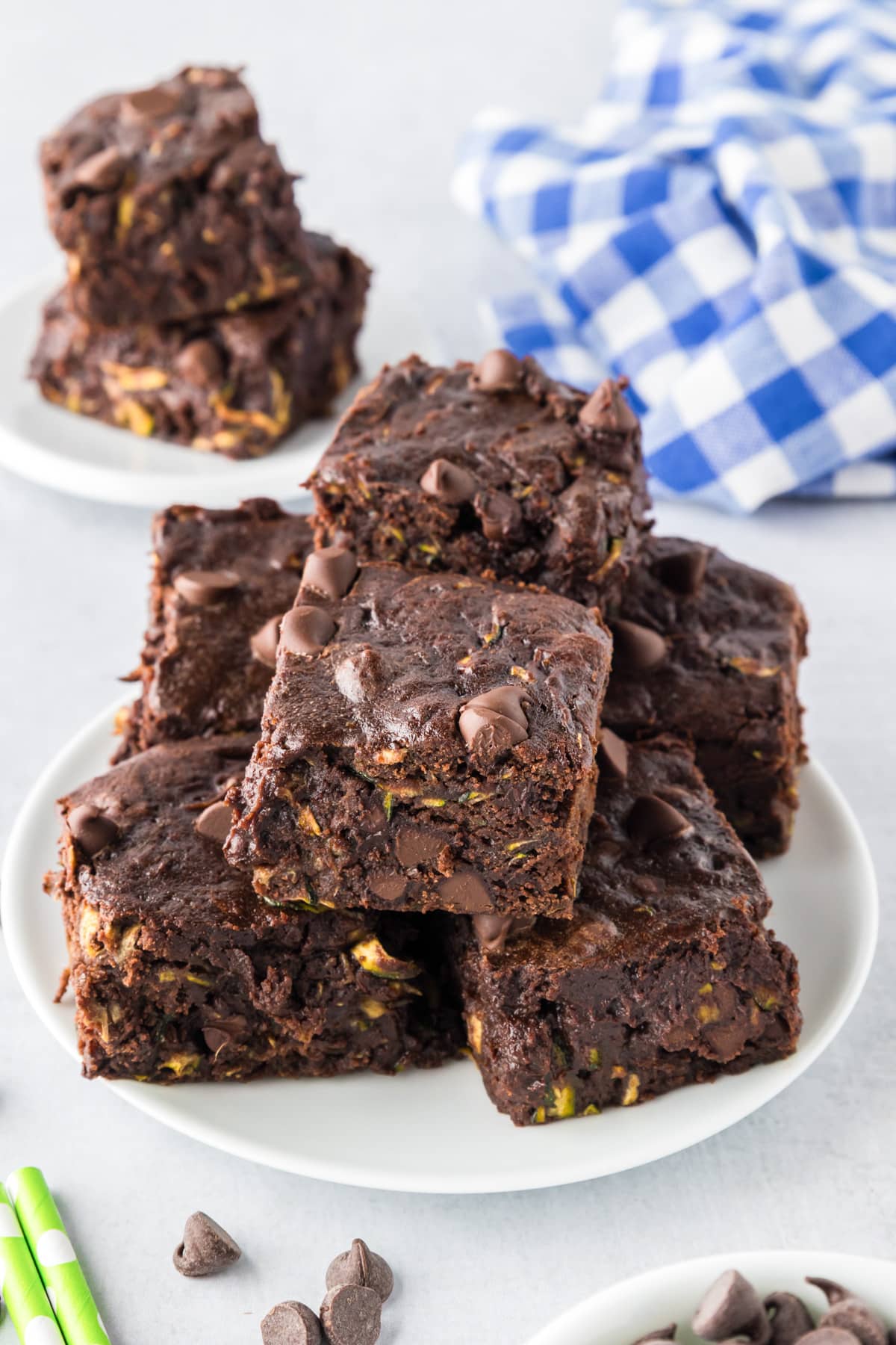 A plate stacked with chocolate zucchini brownies topped with chocolate chip on a table.