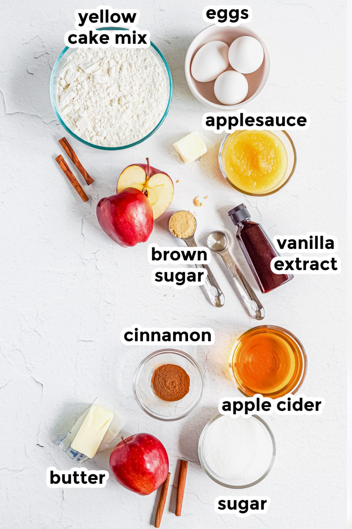 Ingredients for an apple cider donut cake on a counter in bowls with text labels.