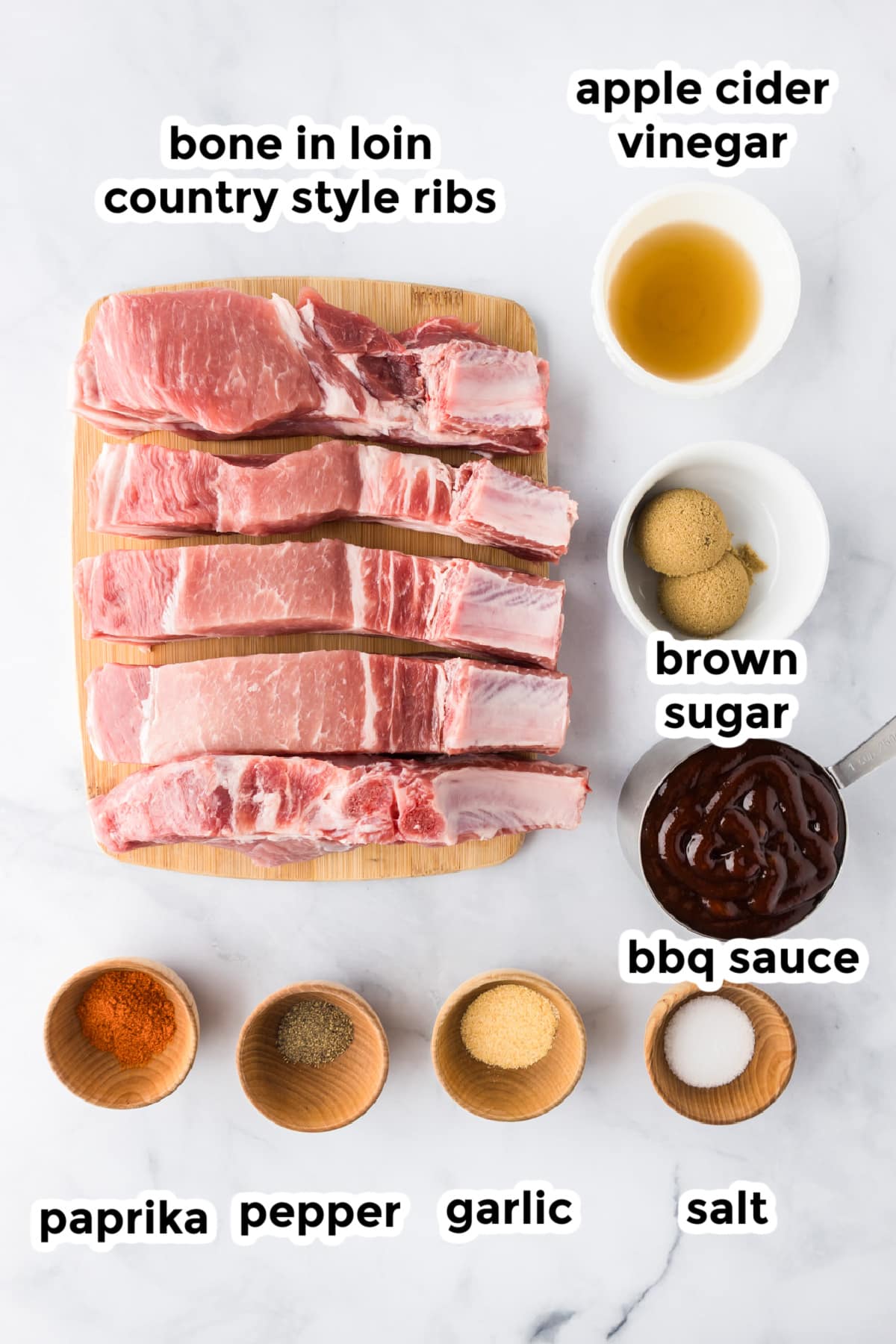 Raw bone-in loin country style ribs are arranged on a cutting board next to more ingredients on a counter in bowls with labels.