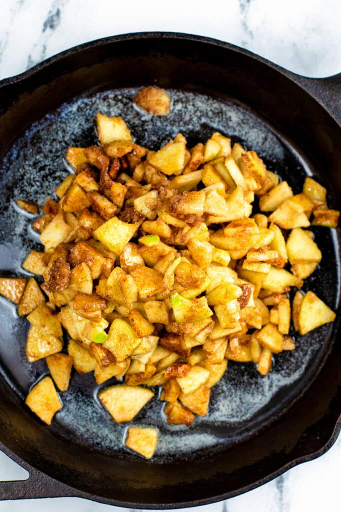 Chopped apples covered in cinnamon and sugar starting to cook in butter in a pan for the filling of apple cookie cups.