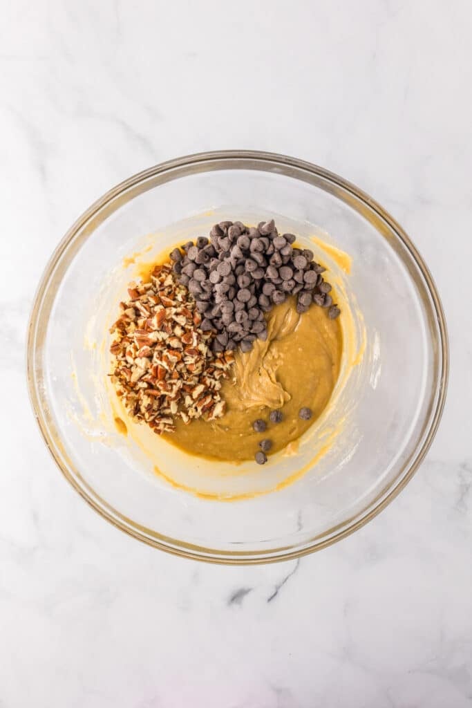 A glass bowl containing blondie batter with pecans and chocolate chips being folded in.