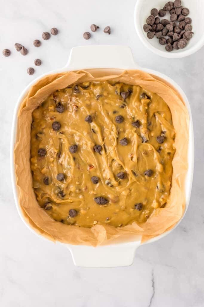 A parchment-lined baking dish filled with unbaked blondie batter sprinkled with chocolate chips.
