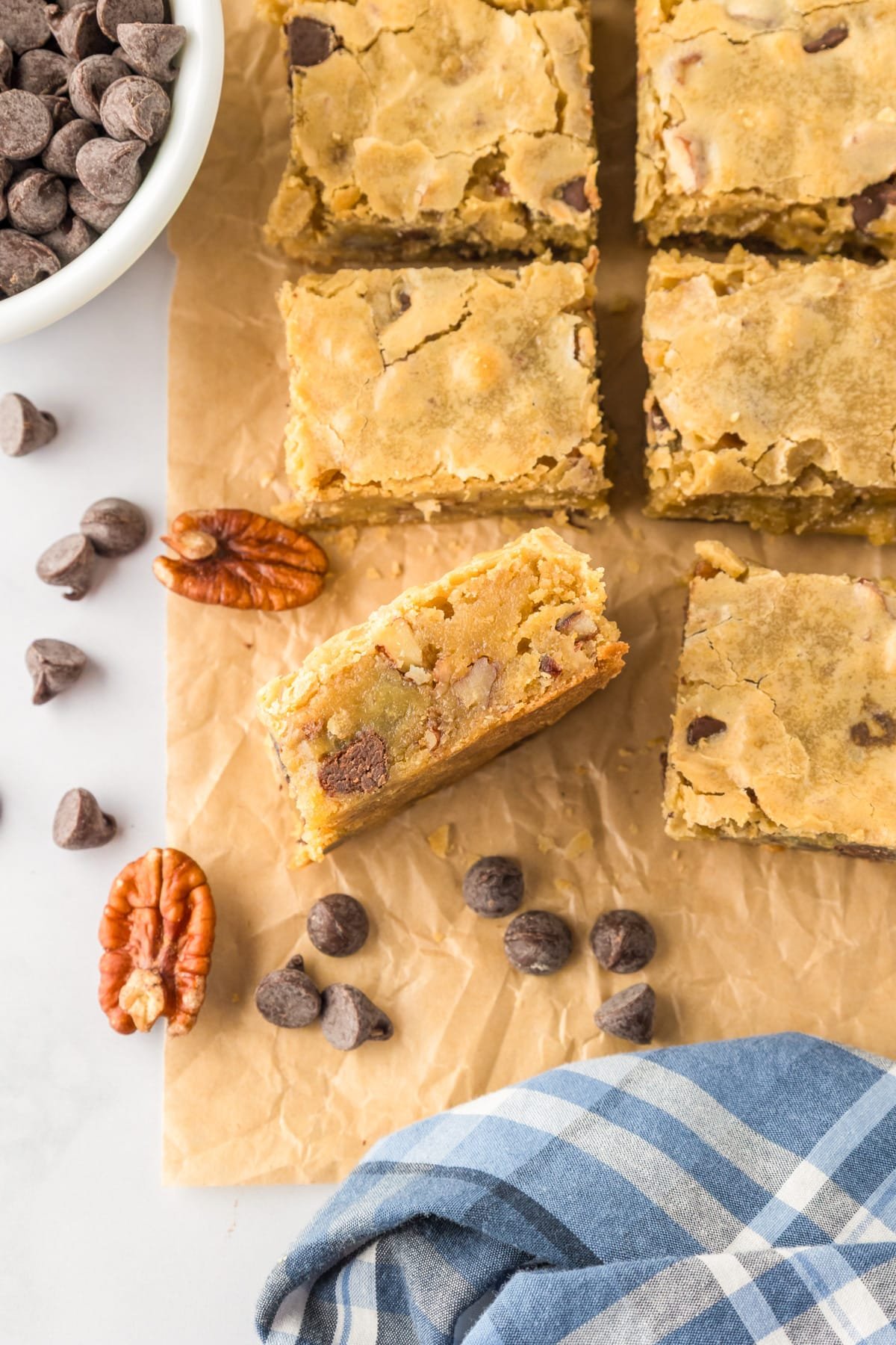 Blondie bars with chocolate chips and pecans on parchment paper sliced with one piece turned to see the thickness of the blondie.