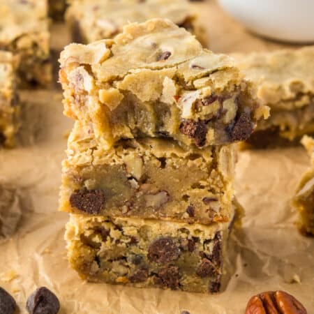 Three stacked blondie bars with chocolate chips and nuts on parchment paper with the top blondie missing a bite.