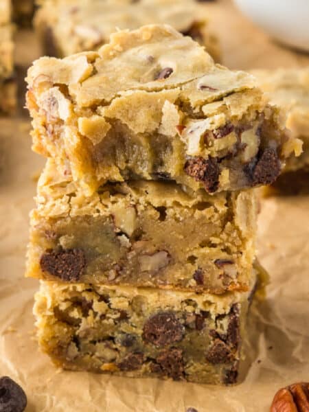 Three stacked blondie bars with chocolate chips and nuts on parchment paper with the top blondie missing a bite.
