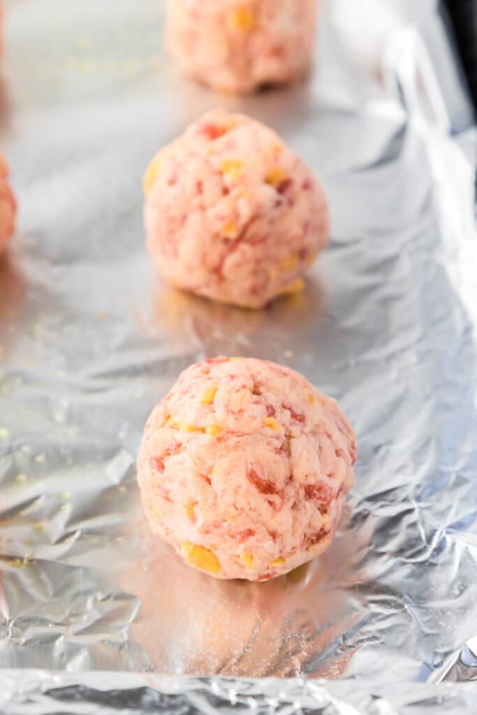 Close up of raw cheddar bay sausage balls lined up on a pan.