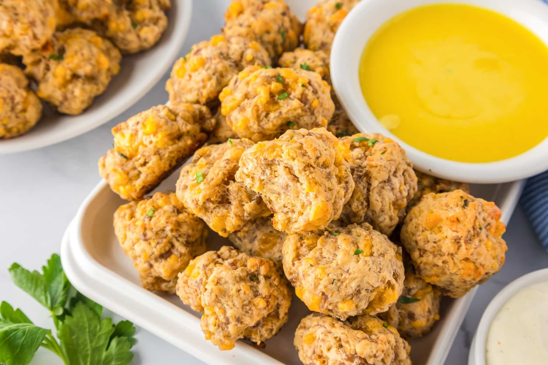A plate of cheddar bay sausage balls next to a bowl of honey mustard dipping sauce, one ball is missing a bite.