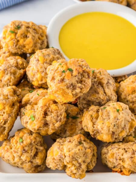 A plate of cheddar bay sausage cheese balls is being served next to a bowl of honey mustard for dipping.
